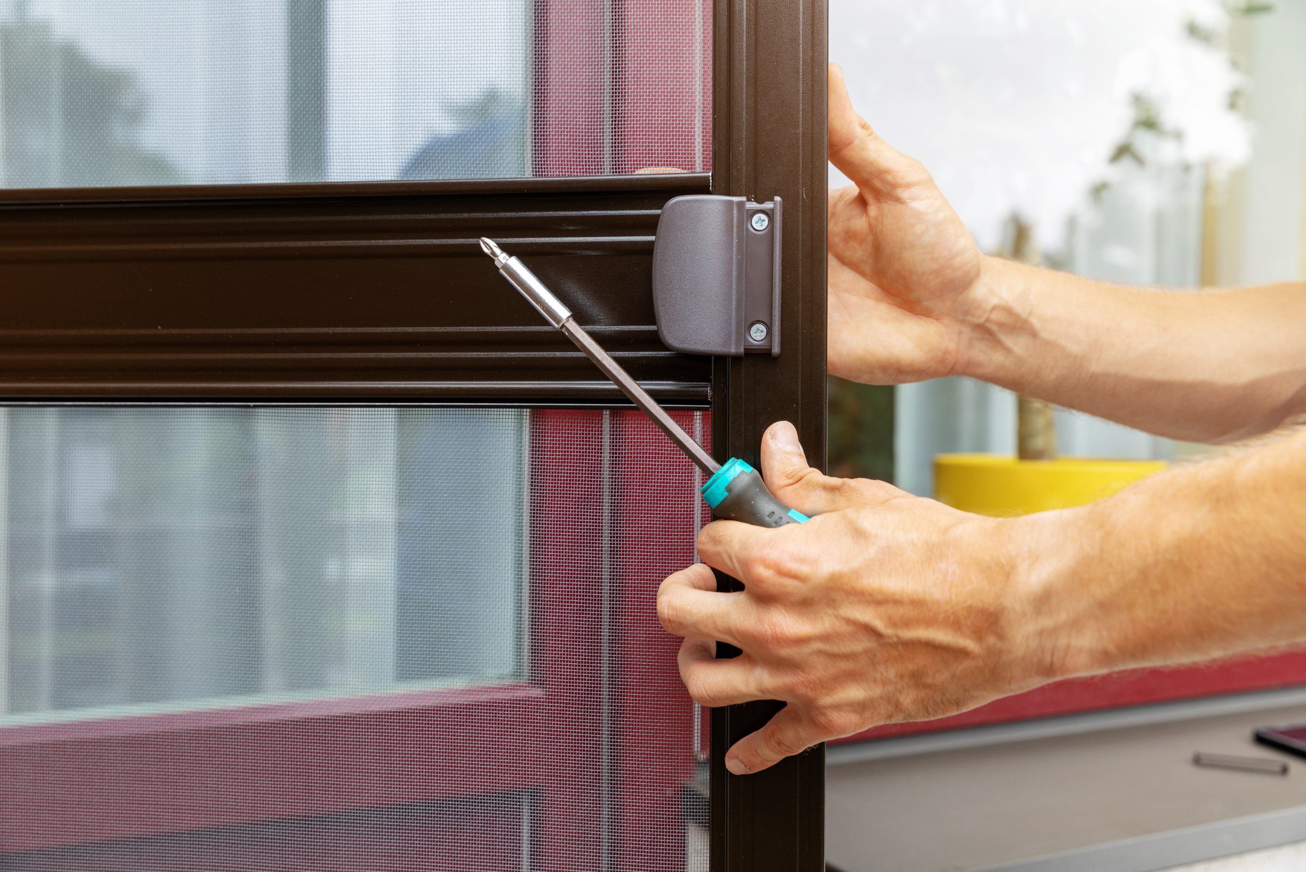 A person's hands holding screen door and screwdriver.