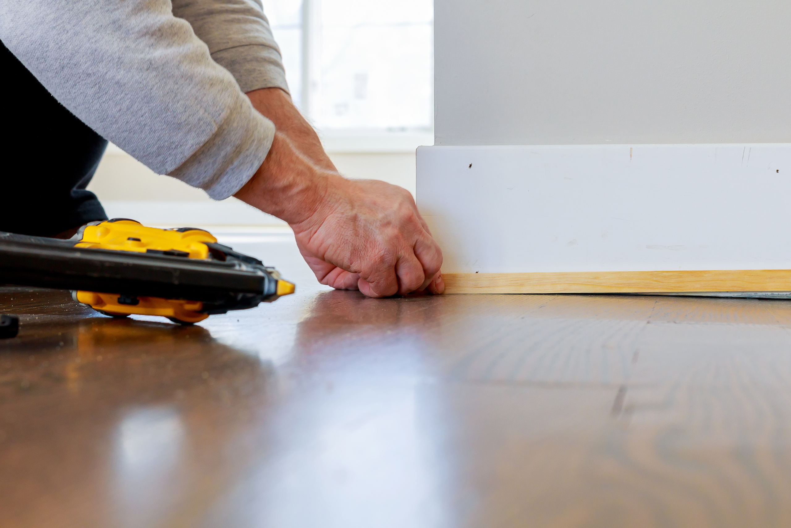 A person using a pin nailer to secure baseboards.