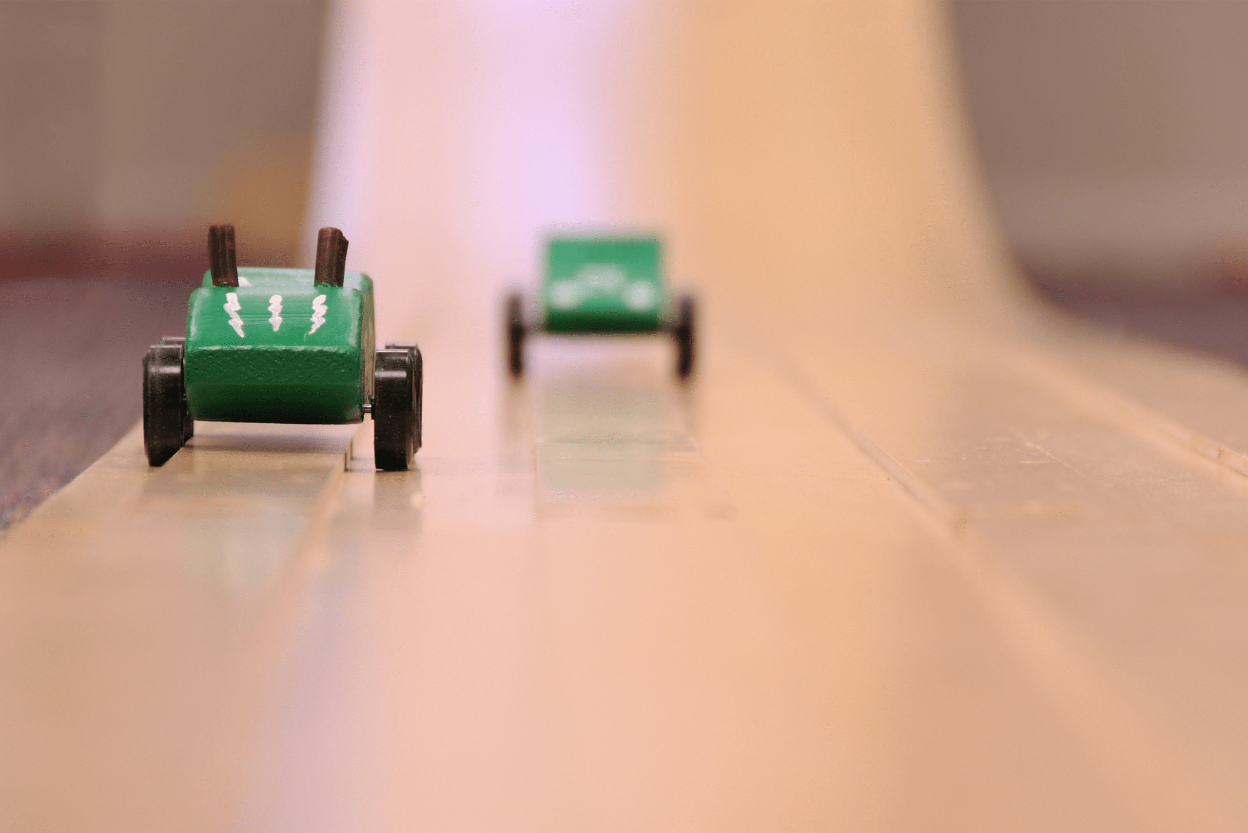 Two green derby cars racing down wooden track.