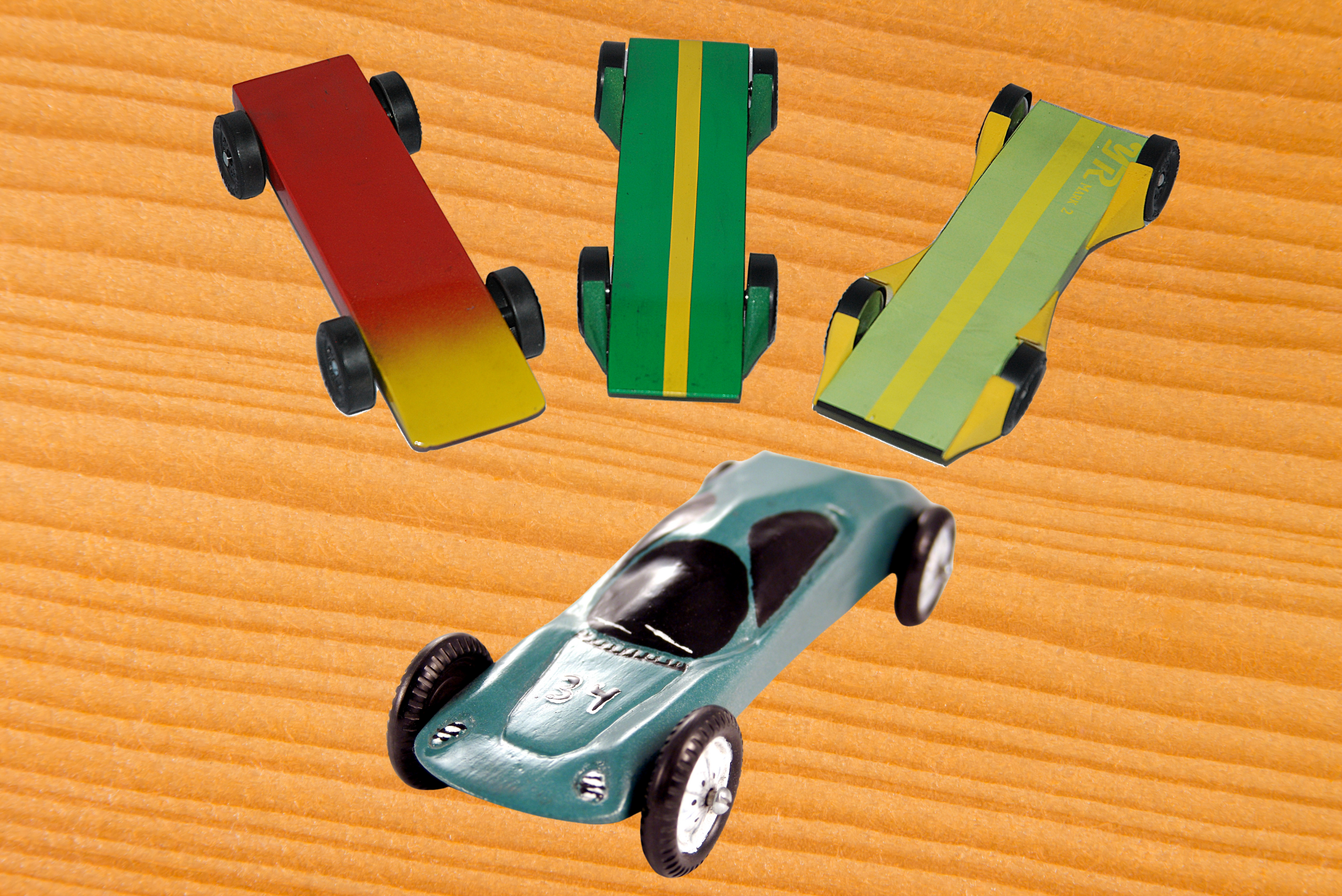 4 pinewood derby car designs on a wooden background.