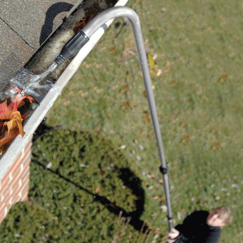 A person using a pressure washer with attachment to clean gutters.