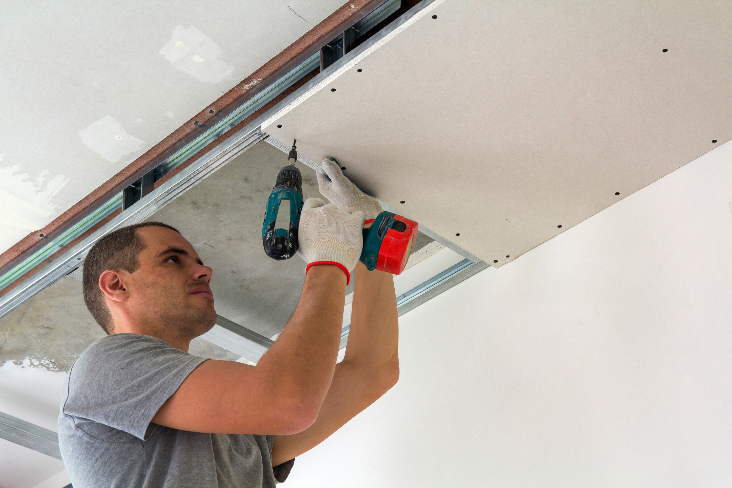 A person using a power drill to screw in drywall sheet to wall.