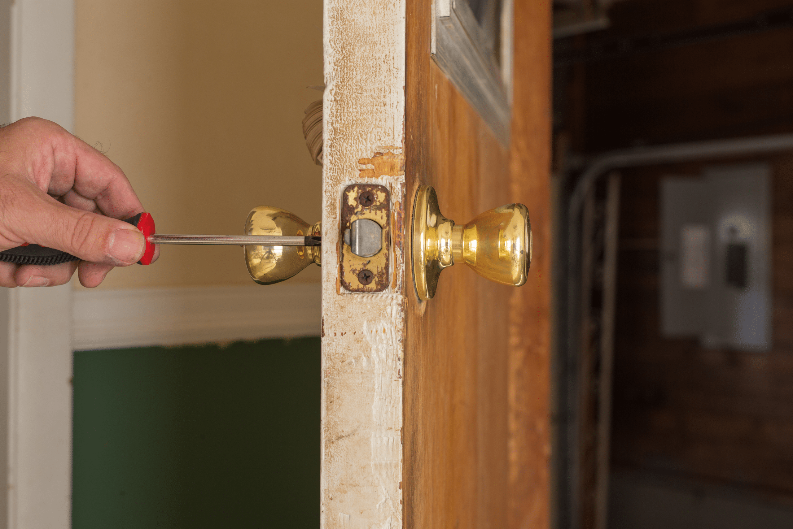 A person using a screwdriver to tighten door knob.