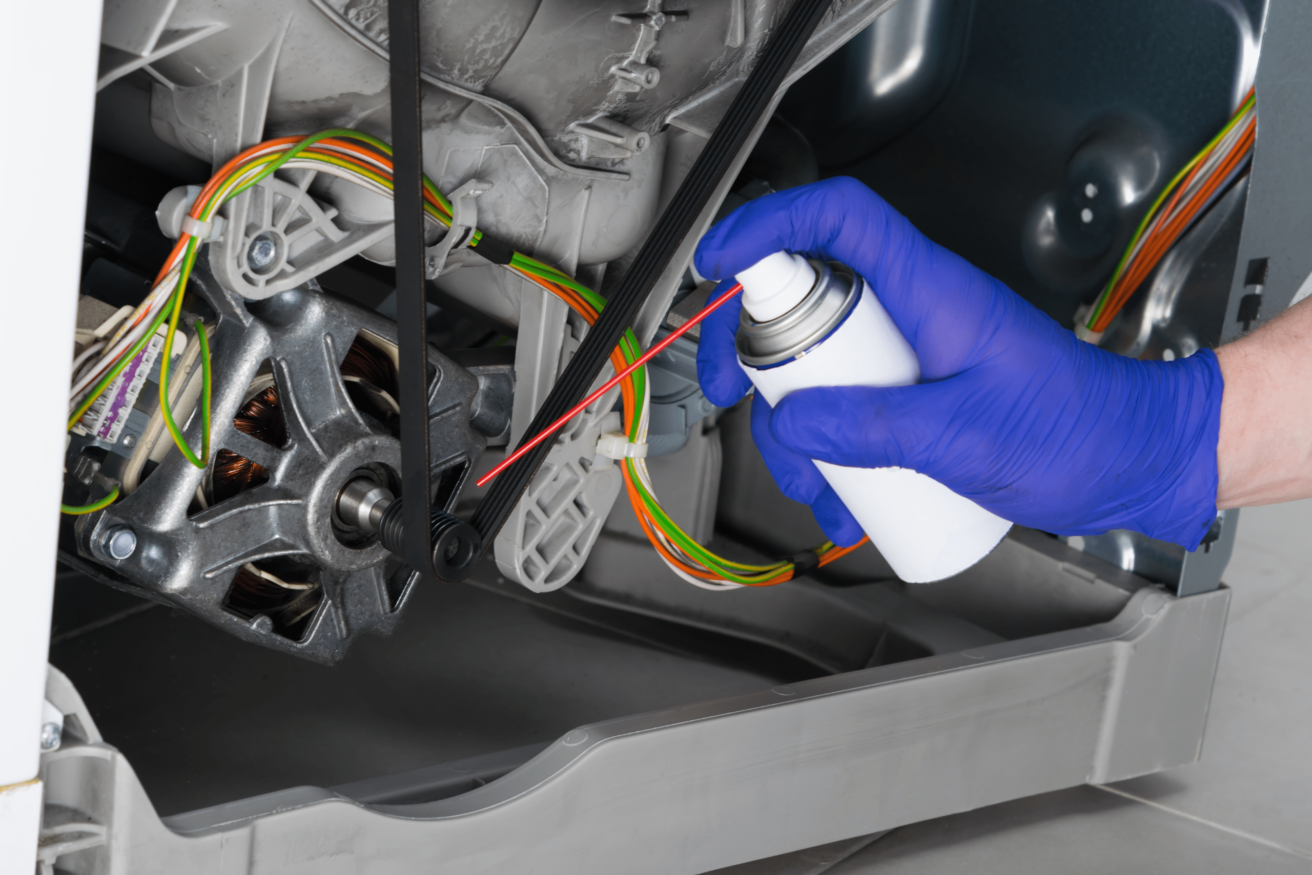 A closeup of a hand wearing blue gloves spraying WD-40 on alternator.