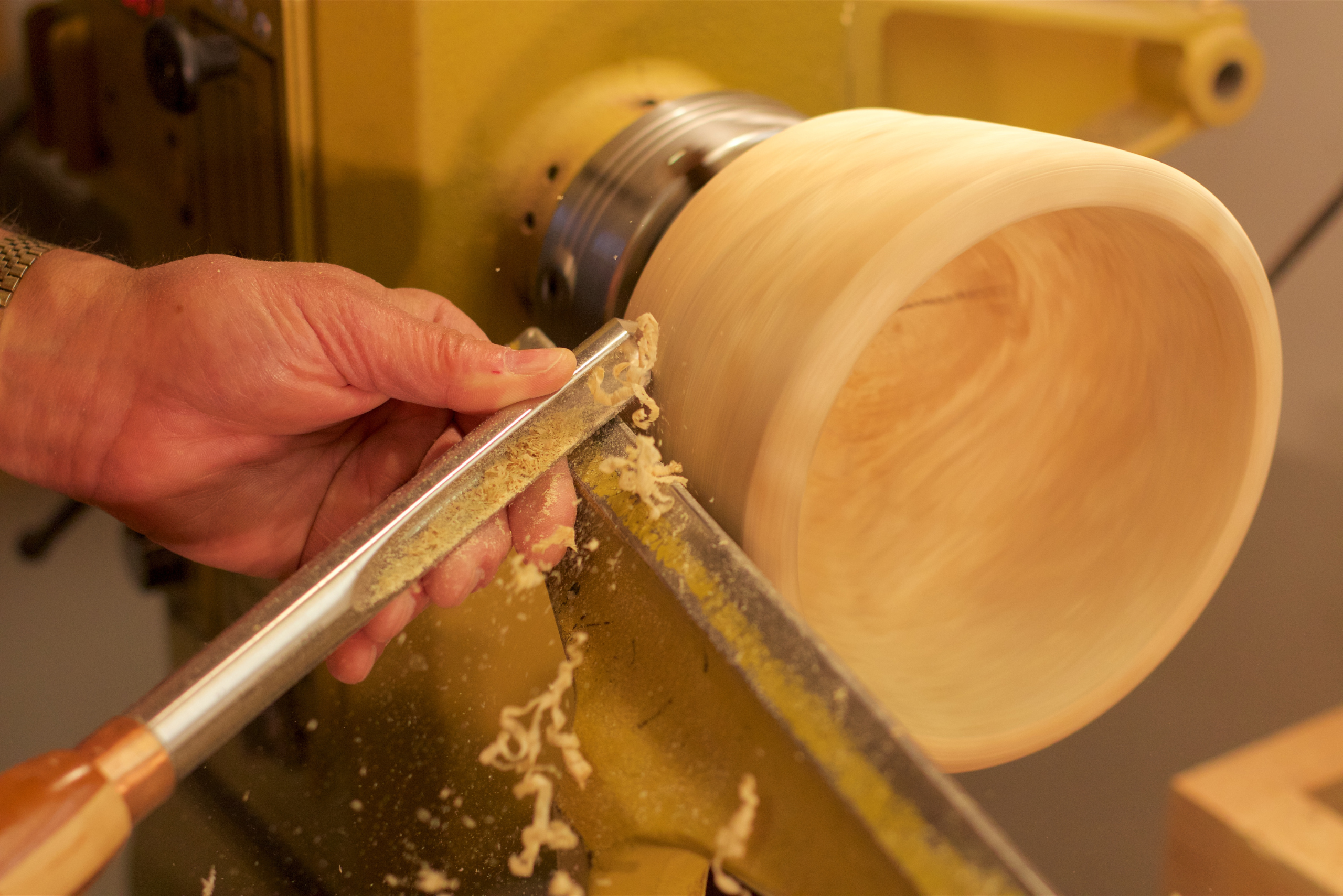 A closeup of someone's hands woodturning a bowl.