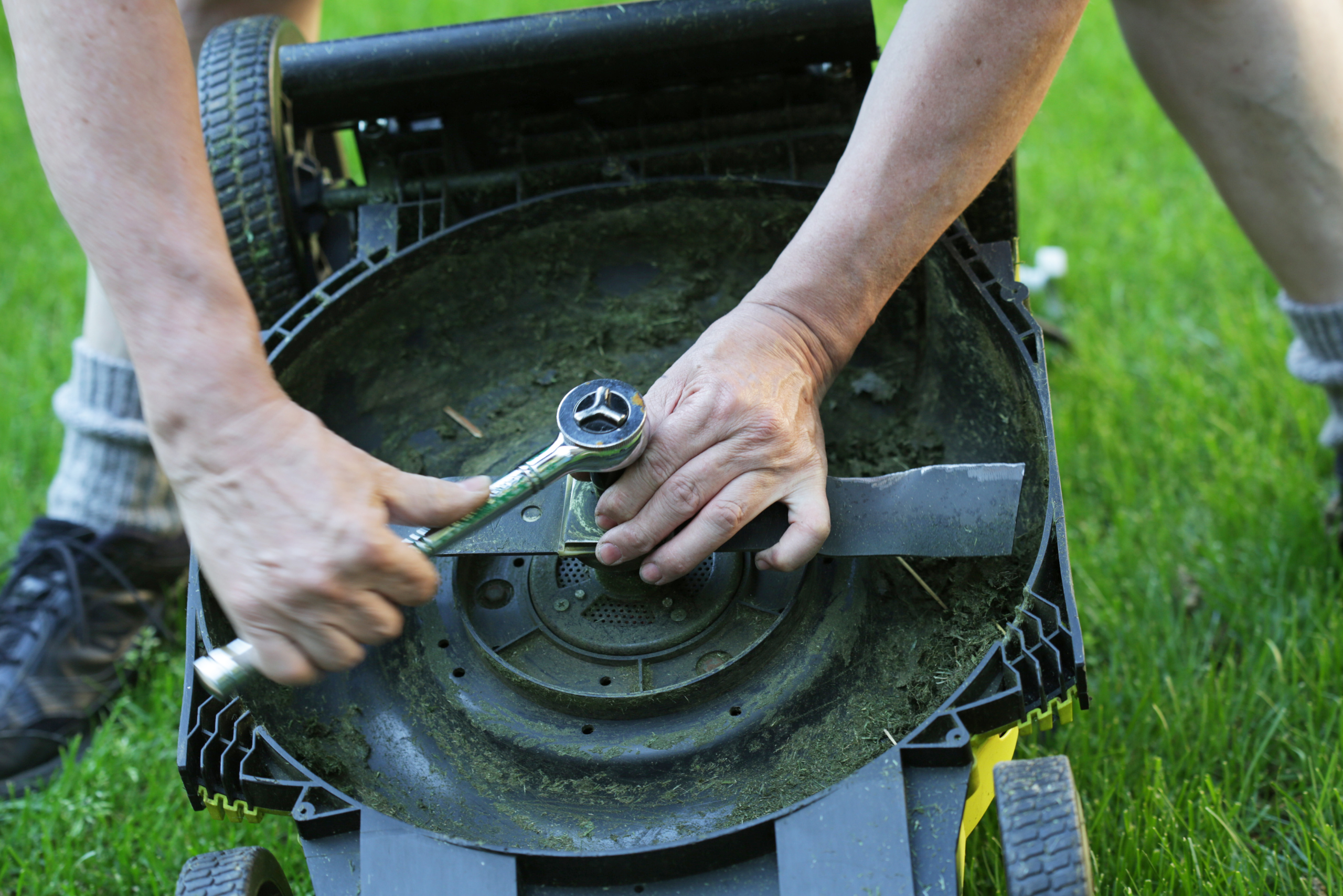 A closeup of someone using a ratchet to remove the nut that holds on lawn mower blade.