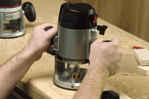 A closeup of someone using a handheld router tool.