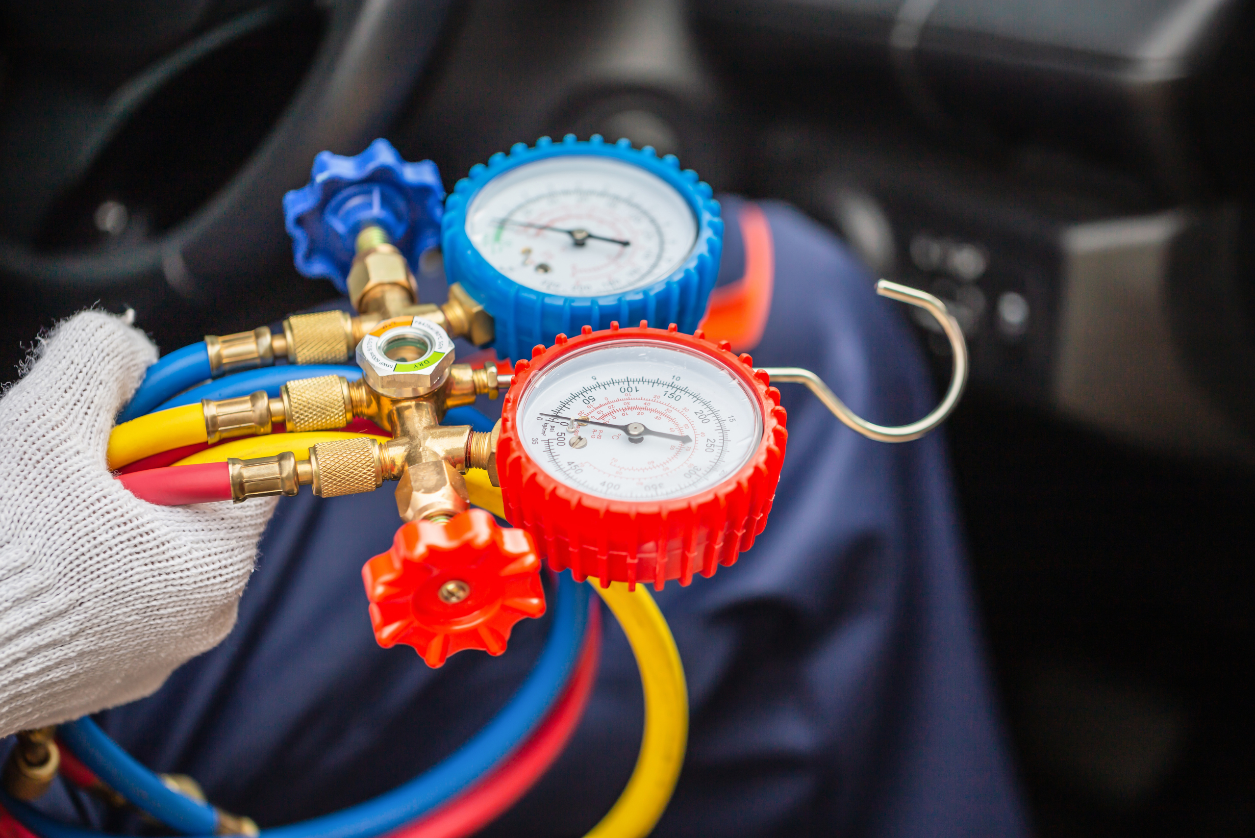 A hand wearing glove holding AC recharging pressure valve.