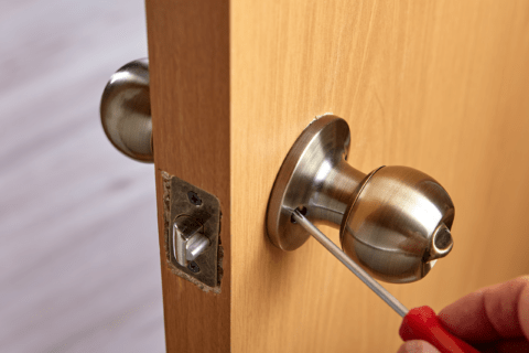 A person using a screwdriver to tighten door knob.