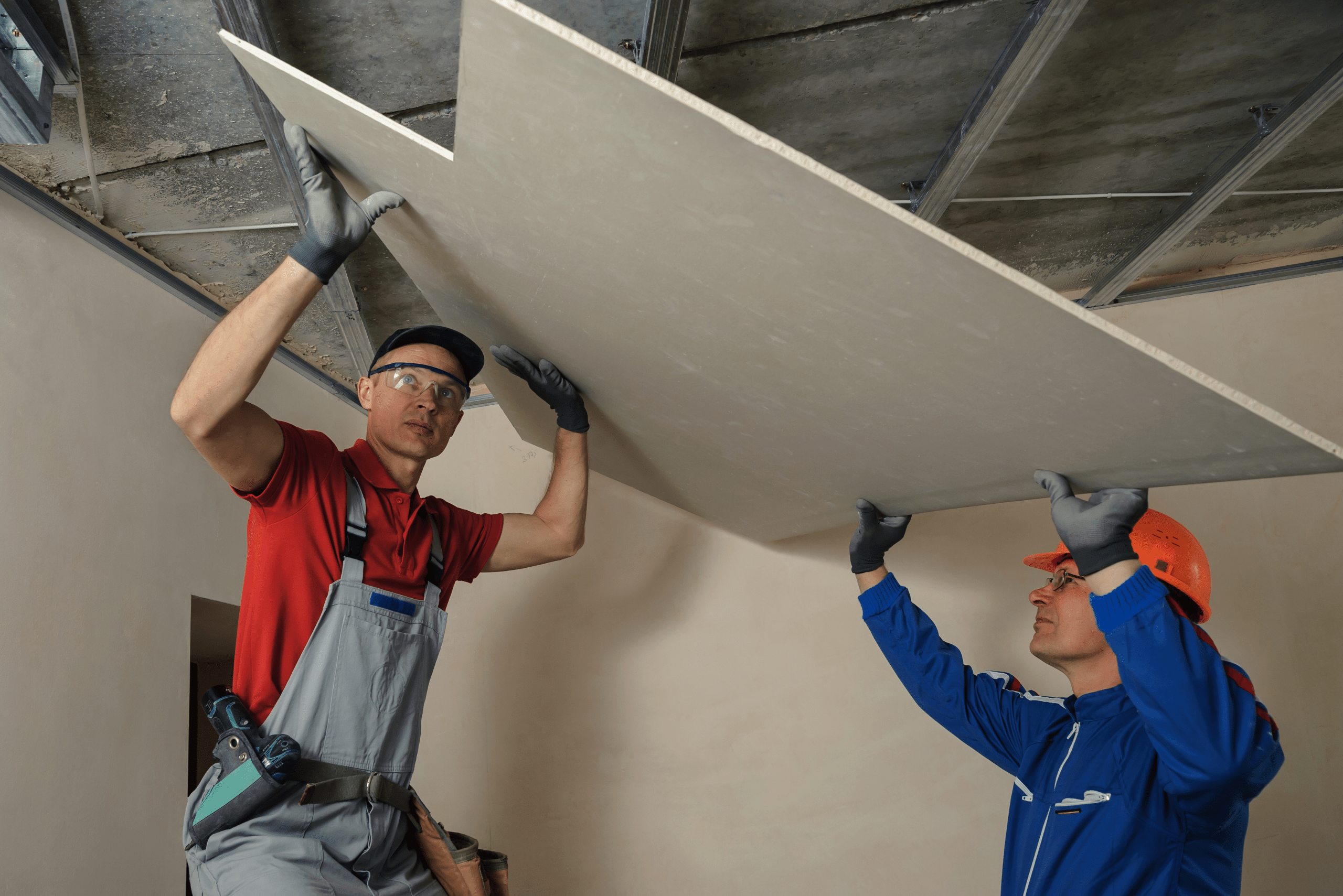 Two people hanging drywall onto metal frames.