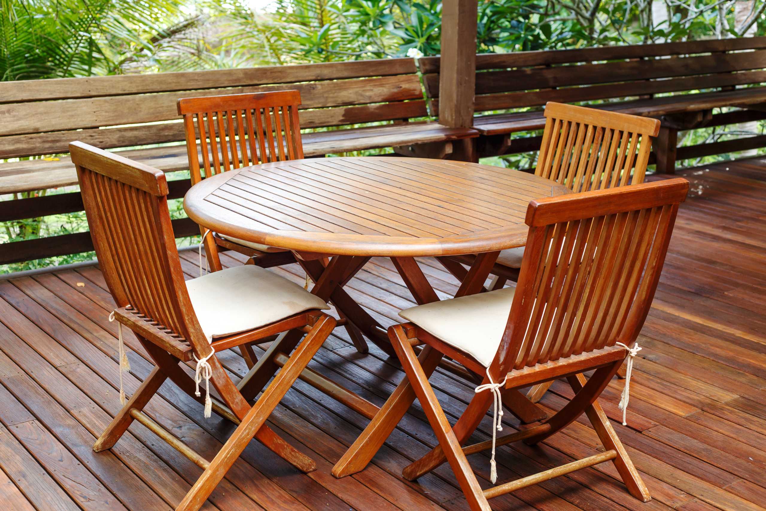 A patio with table and four chairs made of wood and have seat cushions.