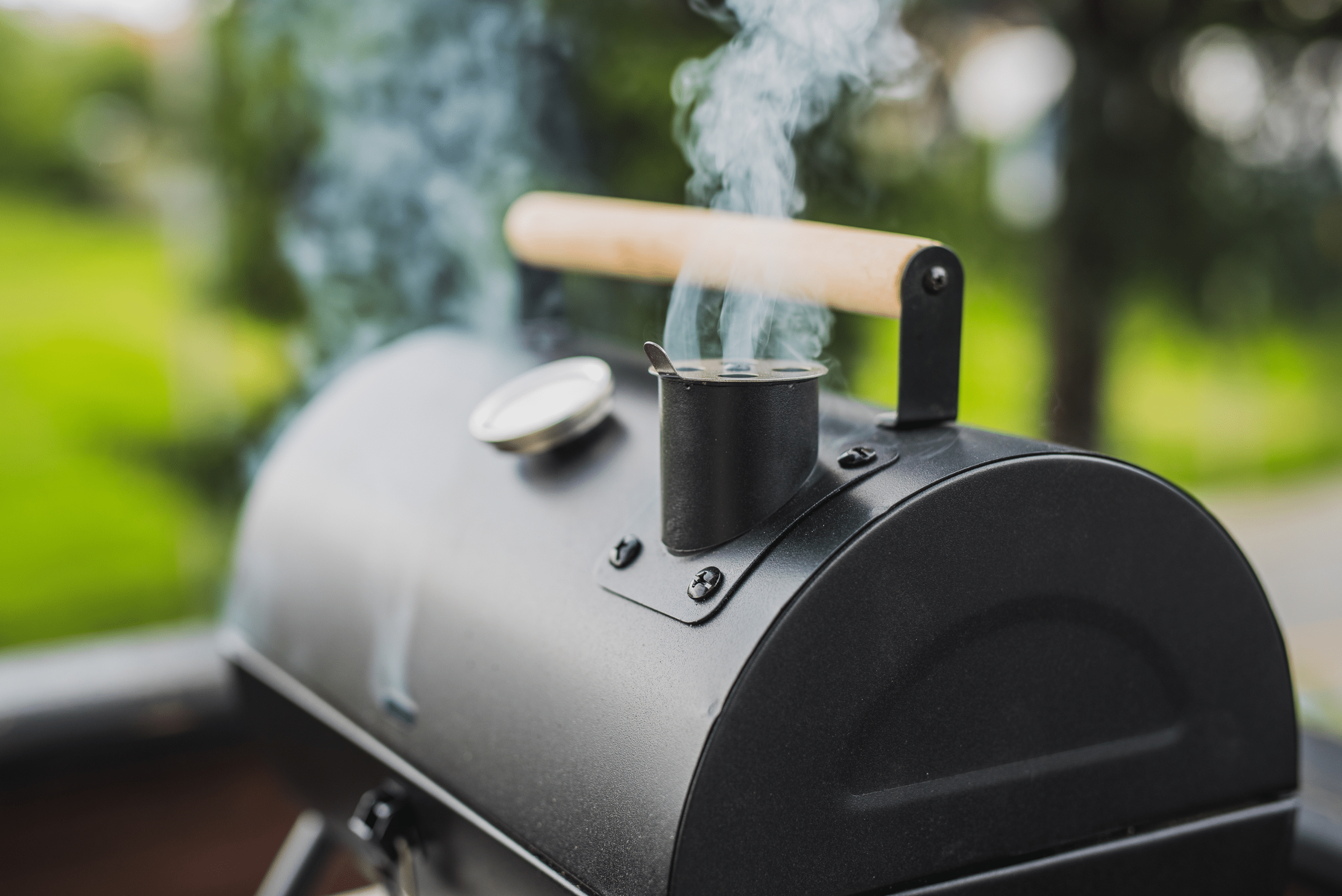 A smoker with wooden handle and smoke coming out of its chimney. 