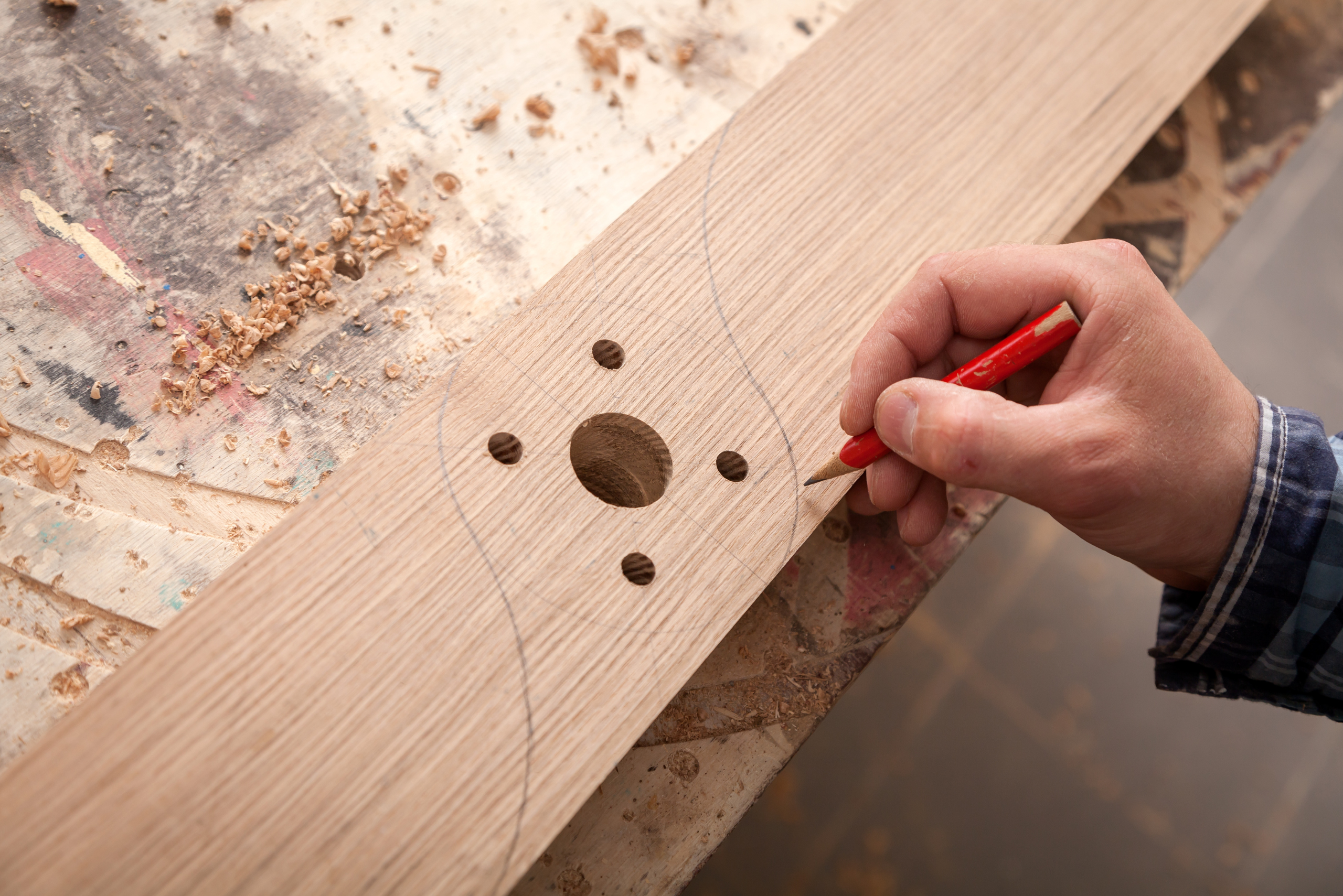 Using a pencil to draw out design onto wooden board that already has multiple holes.