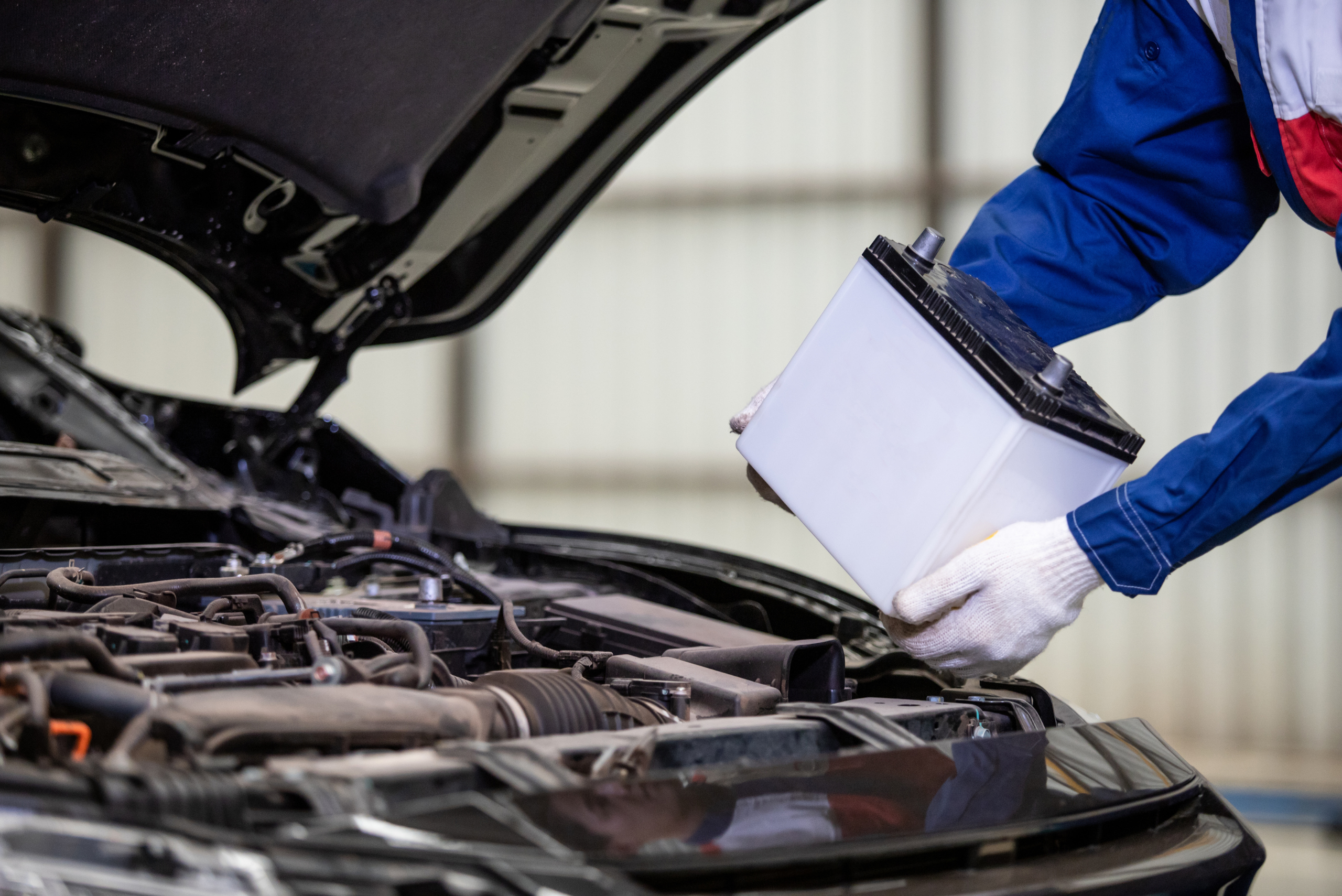 Person removing car battery from under the hood.