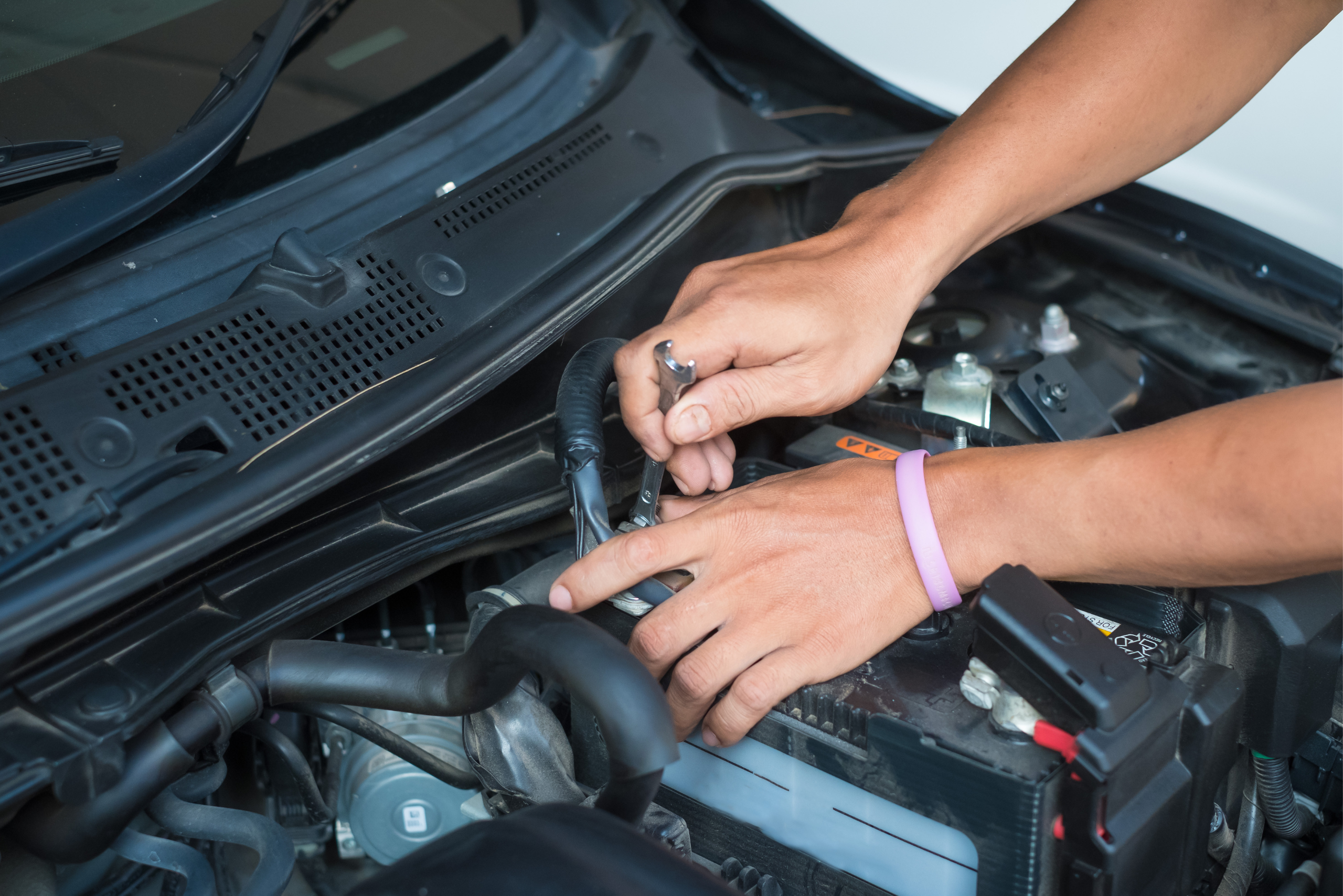 Closeup of someone's hands using a ratchet to loosen battery terminal nuts.