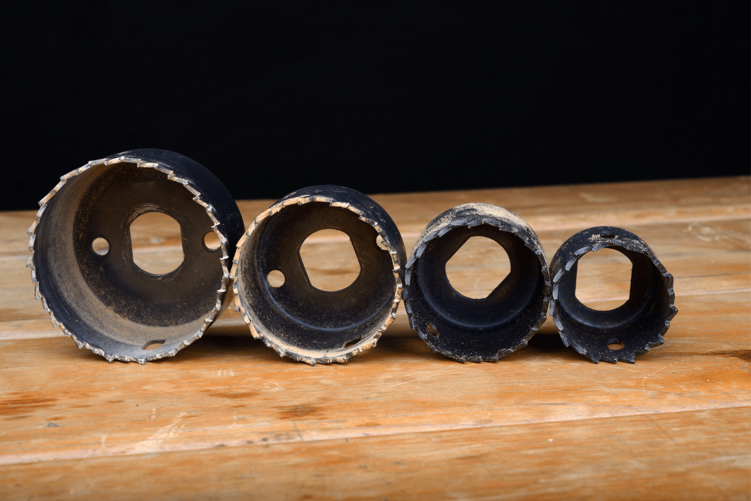 An assortment of hole saw bits on wooden surface.