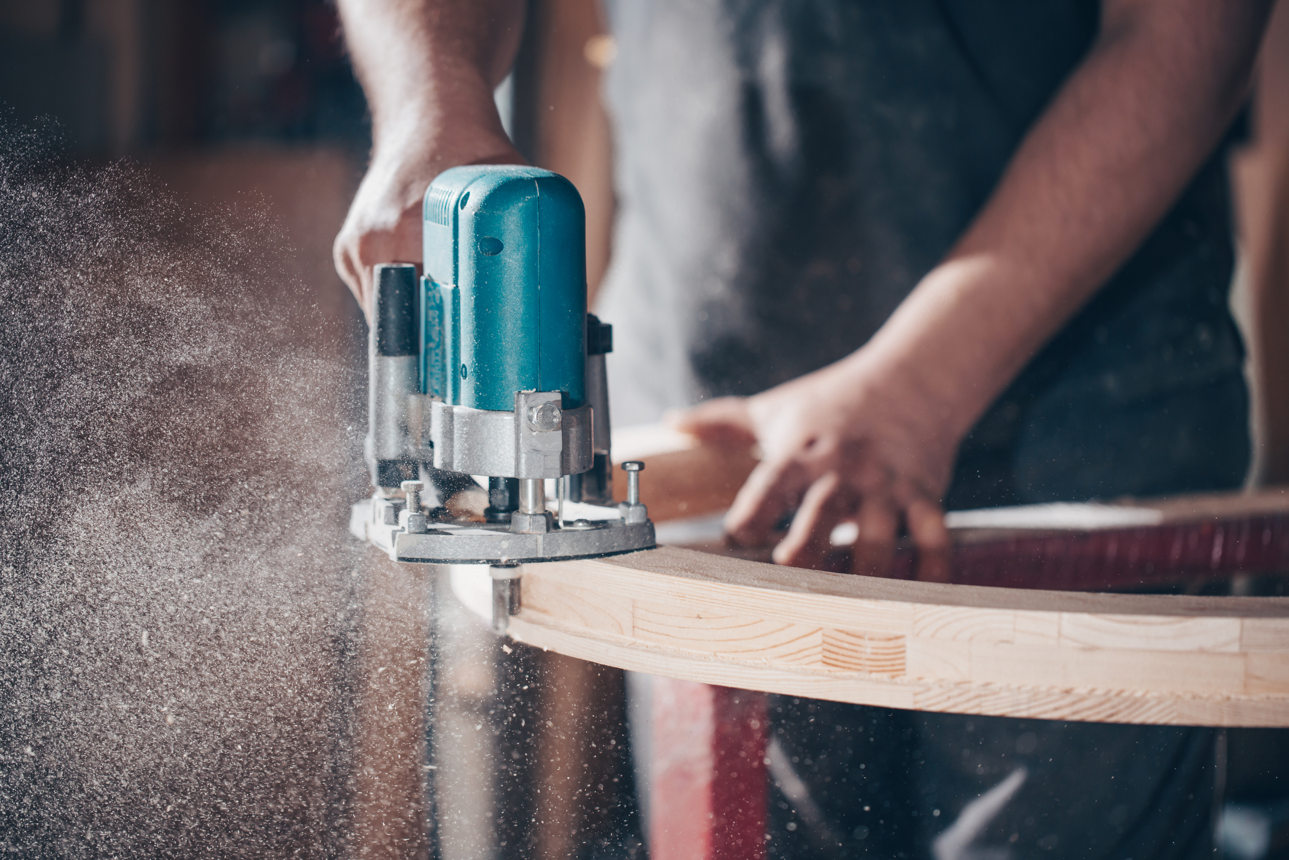 A person using power tool to cut out a tabletop of some sorts.