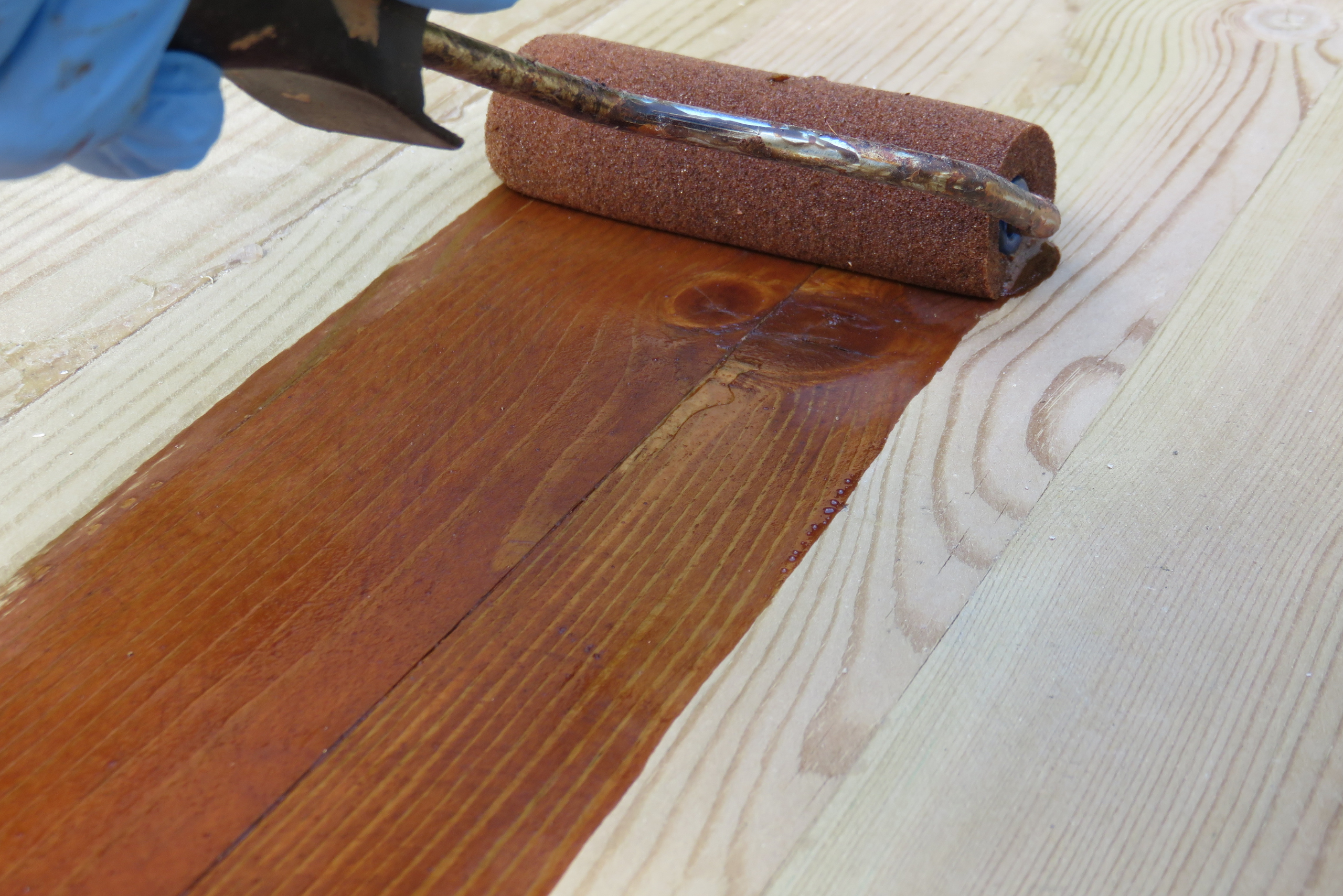 A paint roller being used to apply stain to seal wood.