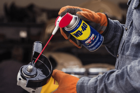 A closeup of someone using WD-40 spray can on an angle grinder.
