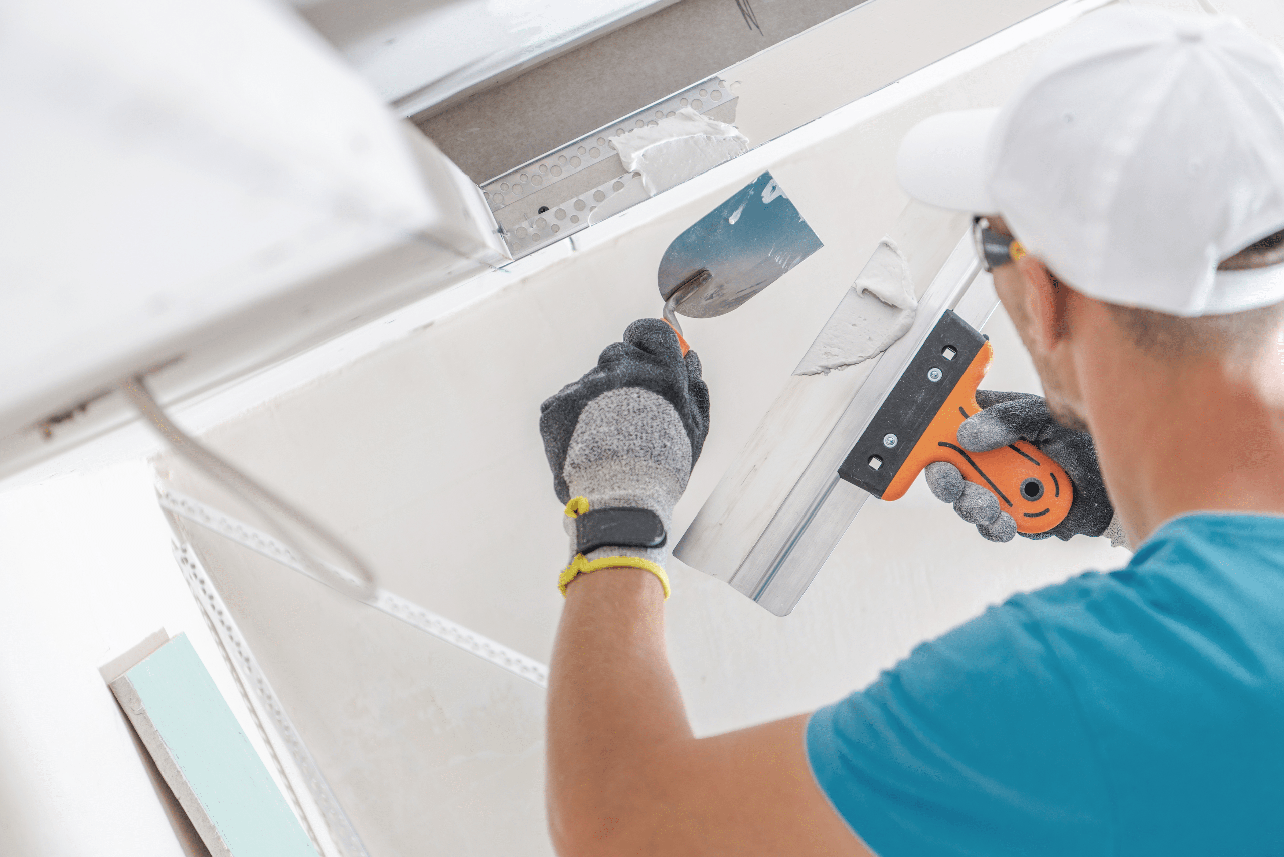 A worker using tools to spread mud onto hung drywall.