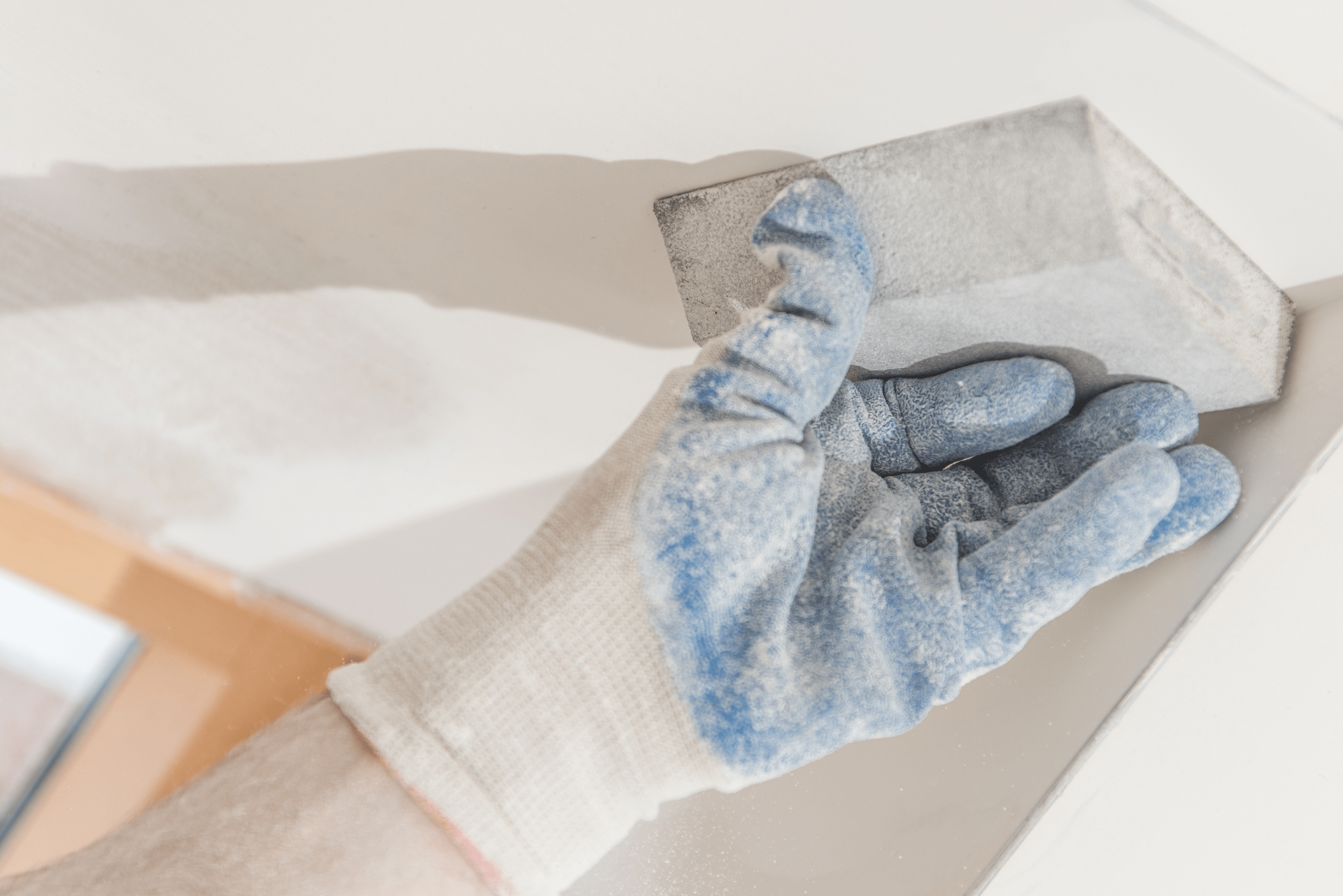 A closeup of a hand using a sanding block to smooth out drywall.