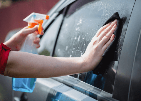 woman wiping car window with microfibre cloth and spray