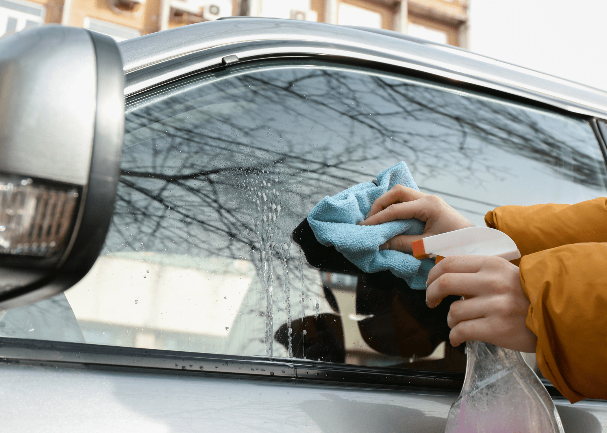 close up of hands wiping car window with cleaner and cloth