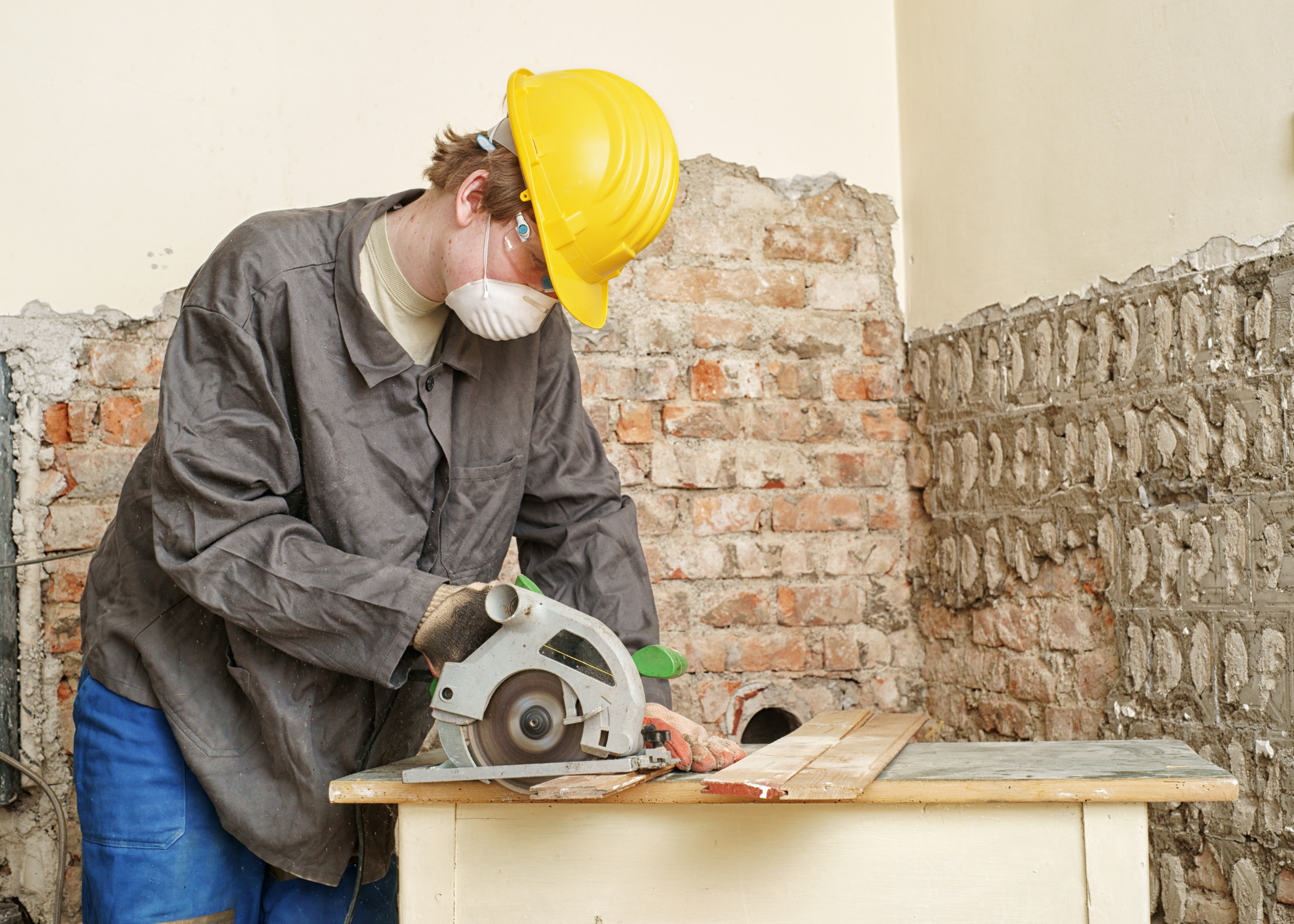 man cutting wood with a circular saw wearing a yellow hard hat