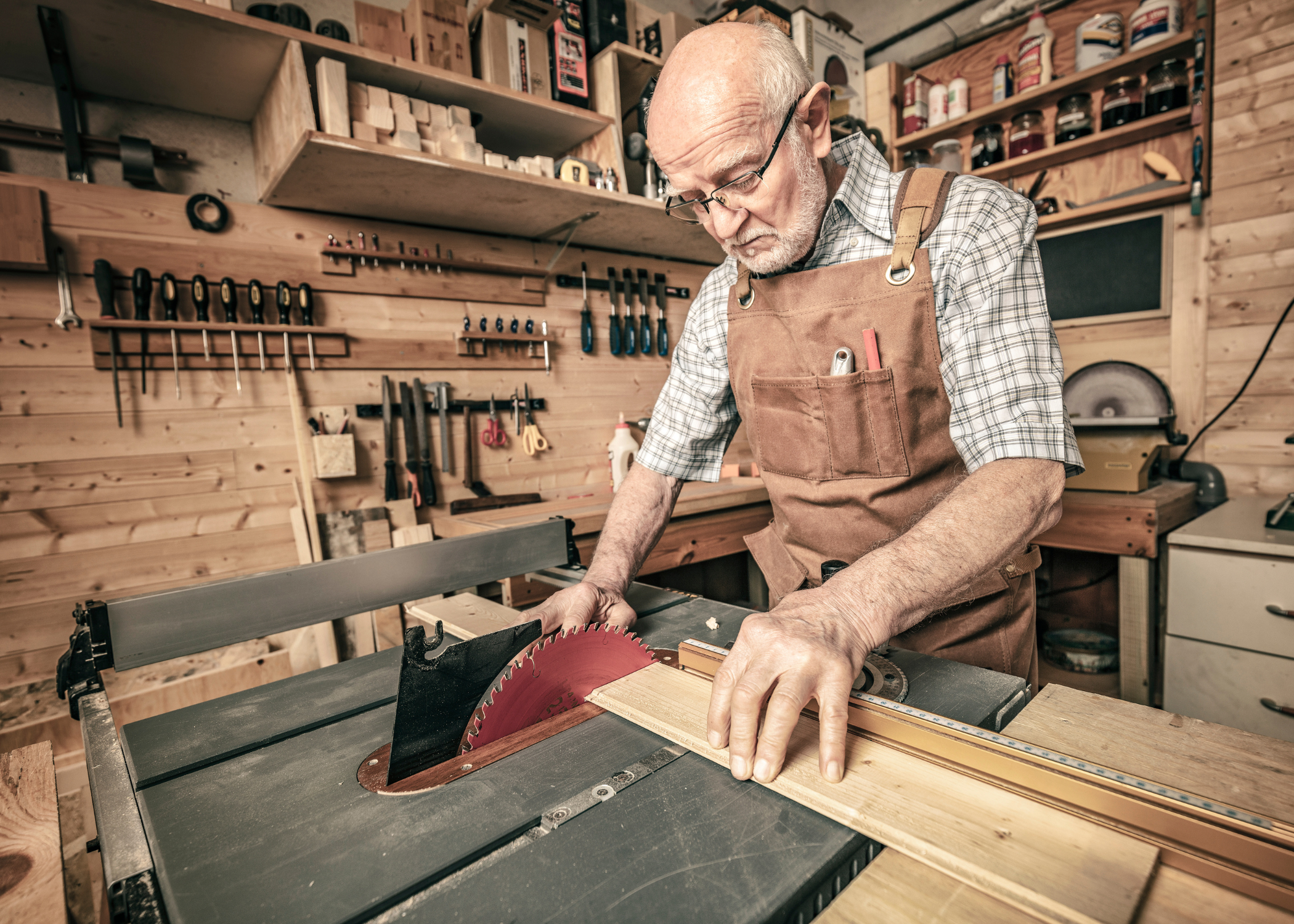 old man cutting wood with a table saw in workshop