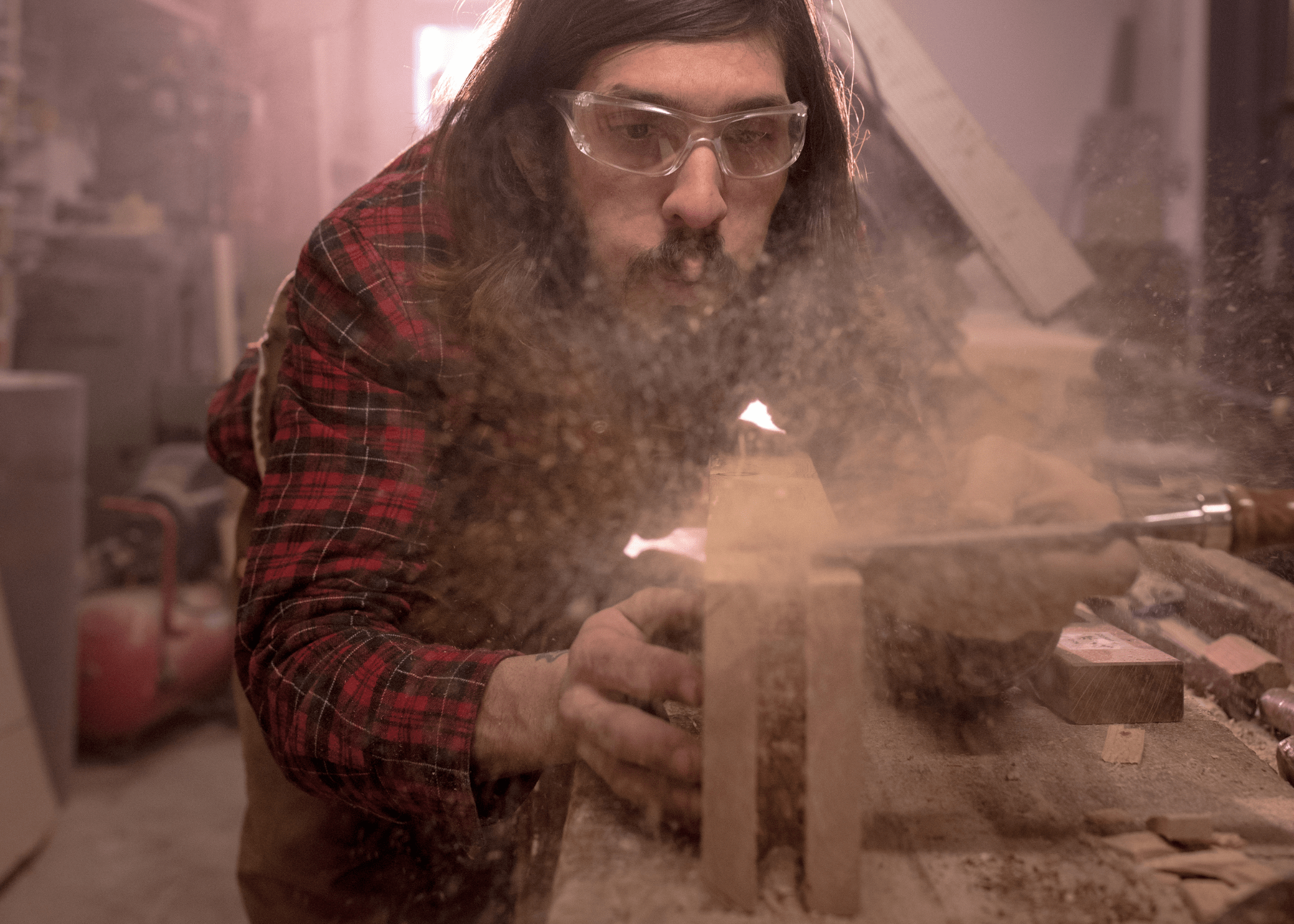 man in workshop blowing dust off wood