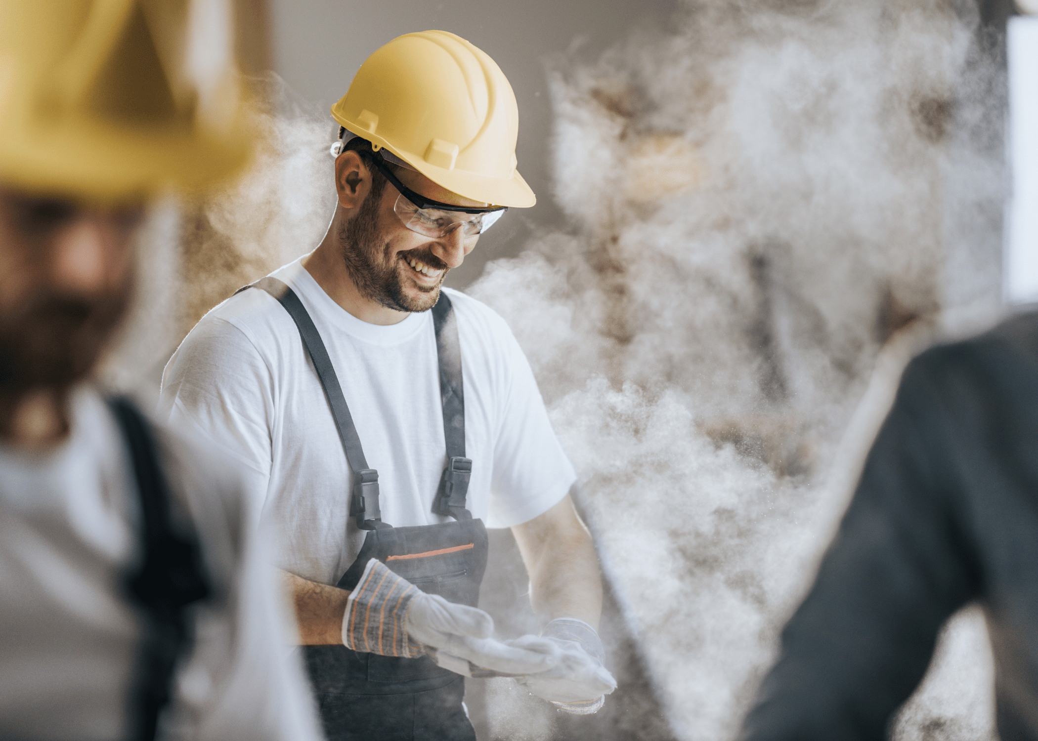 man wearing yellow hard hat wiping dust off his gloves