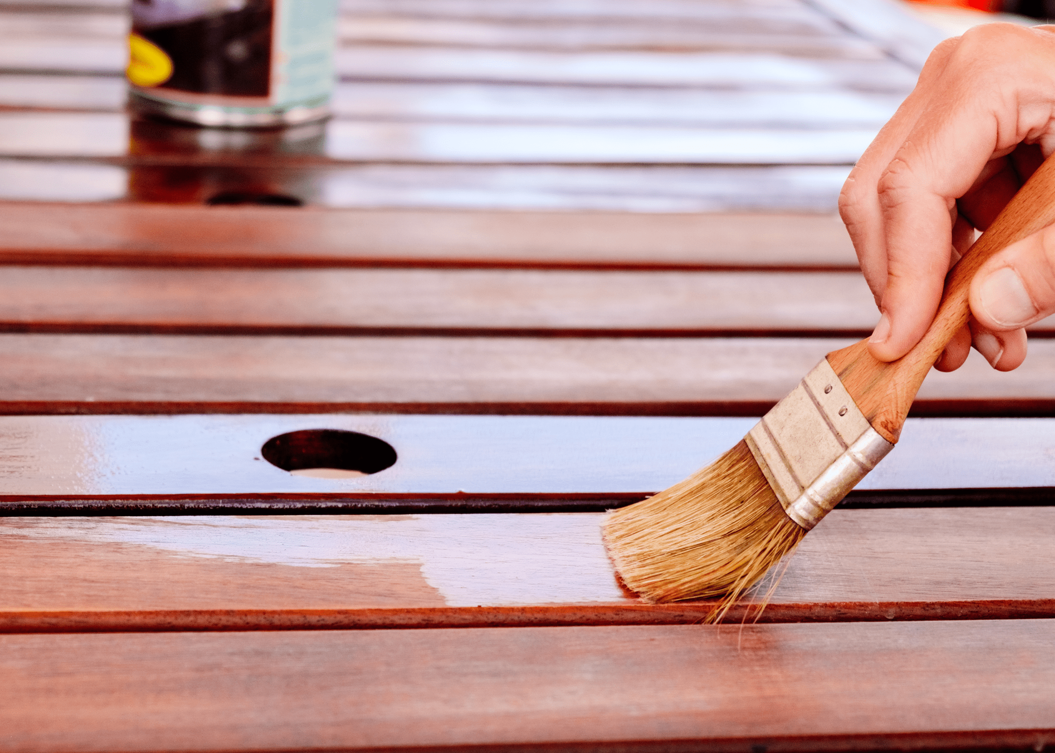 person wiping teak oil on a wood deck