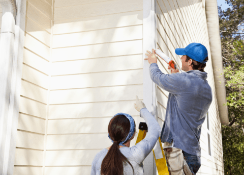 man and woman caulking eavstroph on side of house