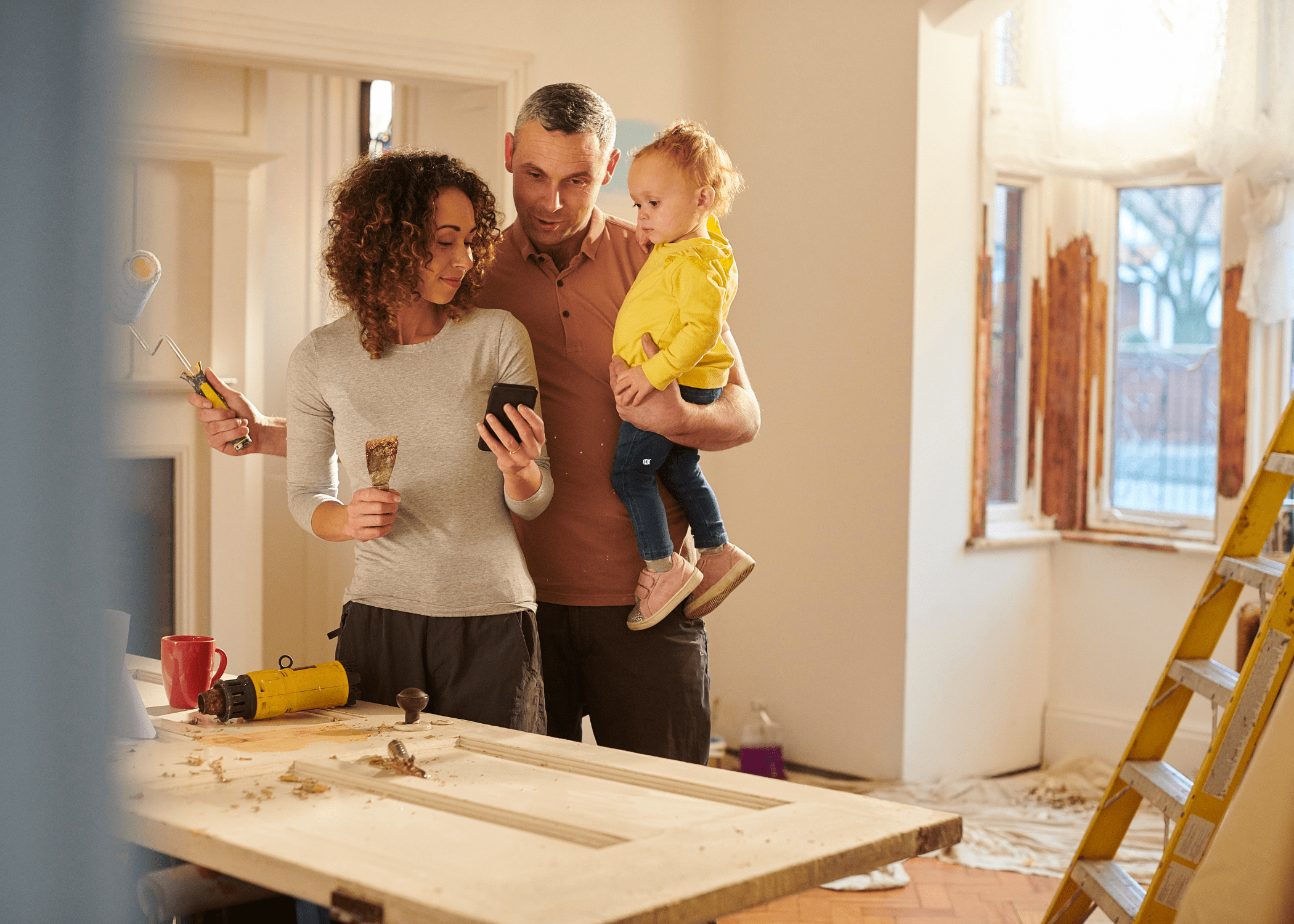 man and woman with child in the middle of house reno looking at phone