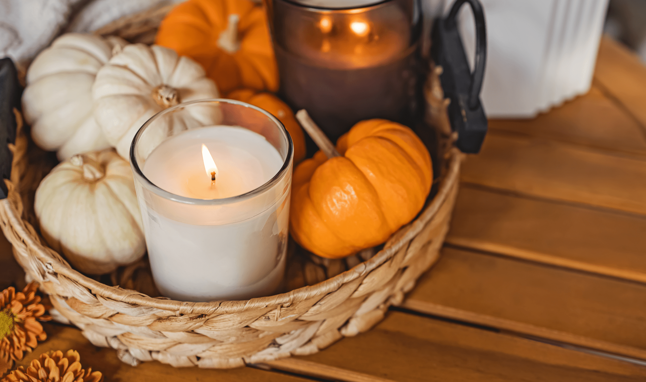 A small basket of fall decor items, some candles and small pumpkins.