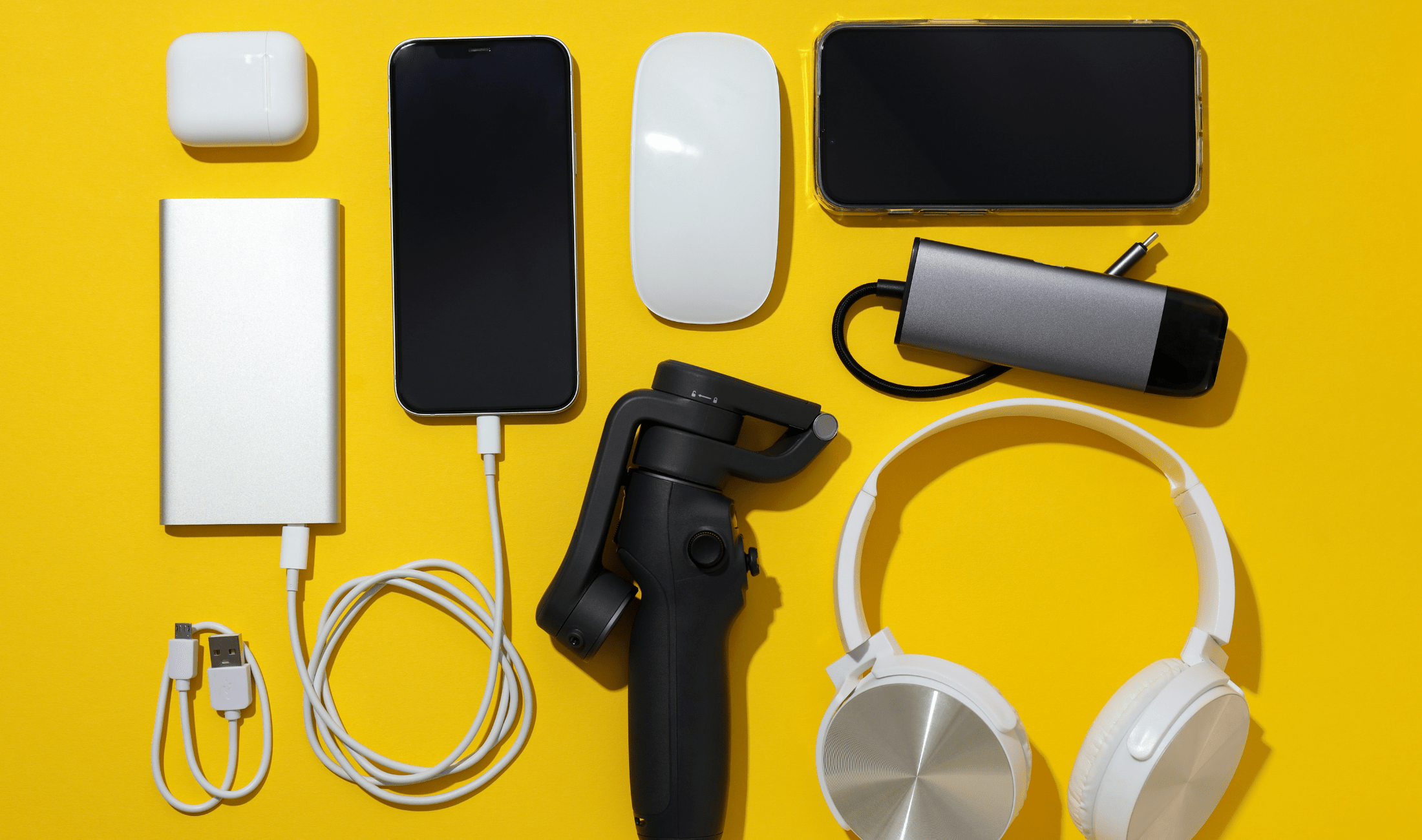 A yellow backdrop with an organized layout of some smart phones and their various accessories.