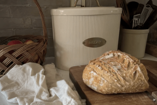 Bread box with loaf of bread on cutting board.