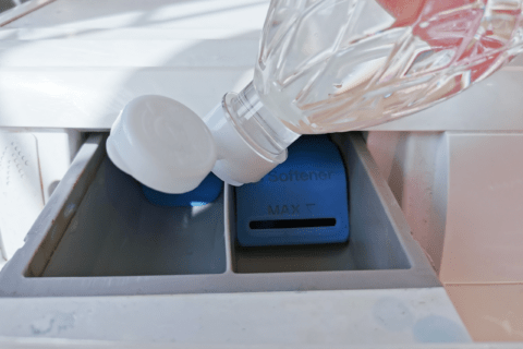Pouring white vinegar into washing machine drawer.