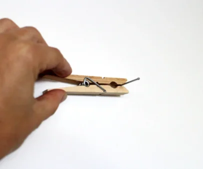 Someone using a clothespin to hold a nail against the wall.