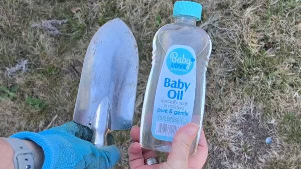 Someone holding a bottle of baby oil next to a garden spade.
