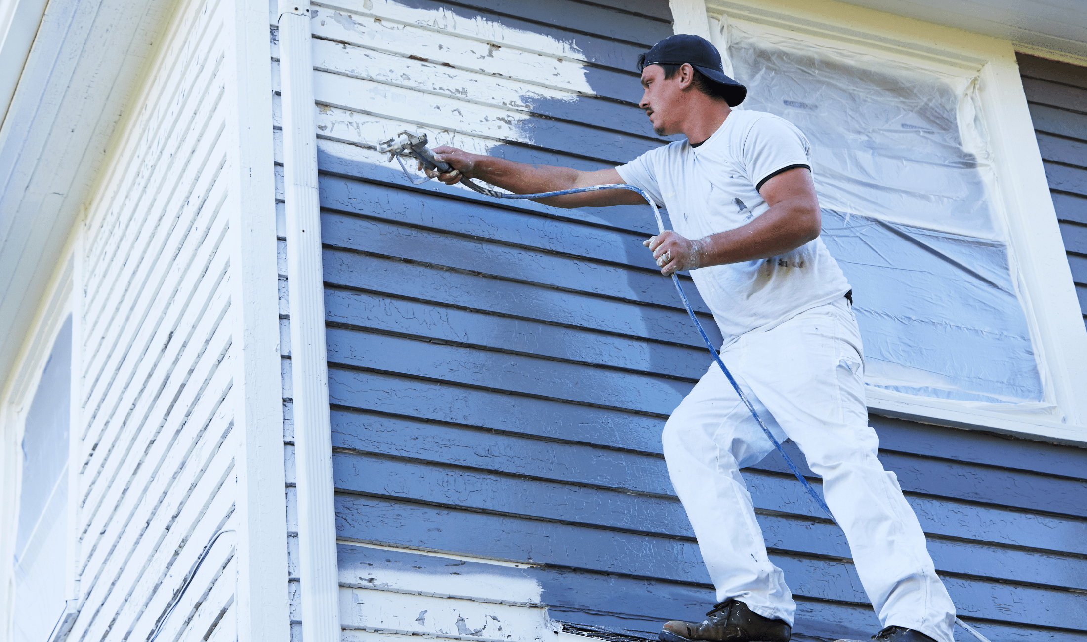 A man standing on a patio roof painting a wall grey.
