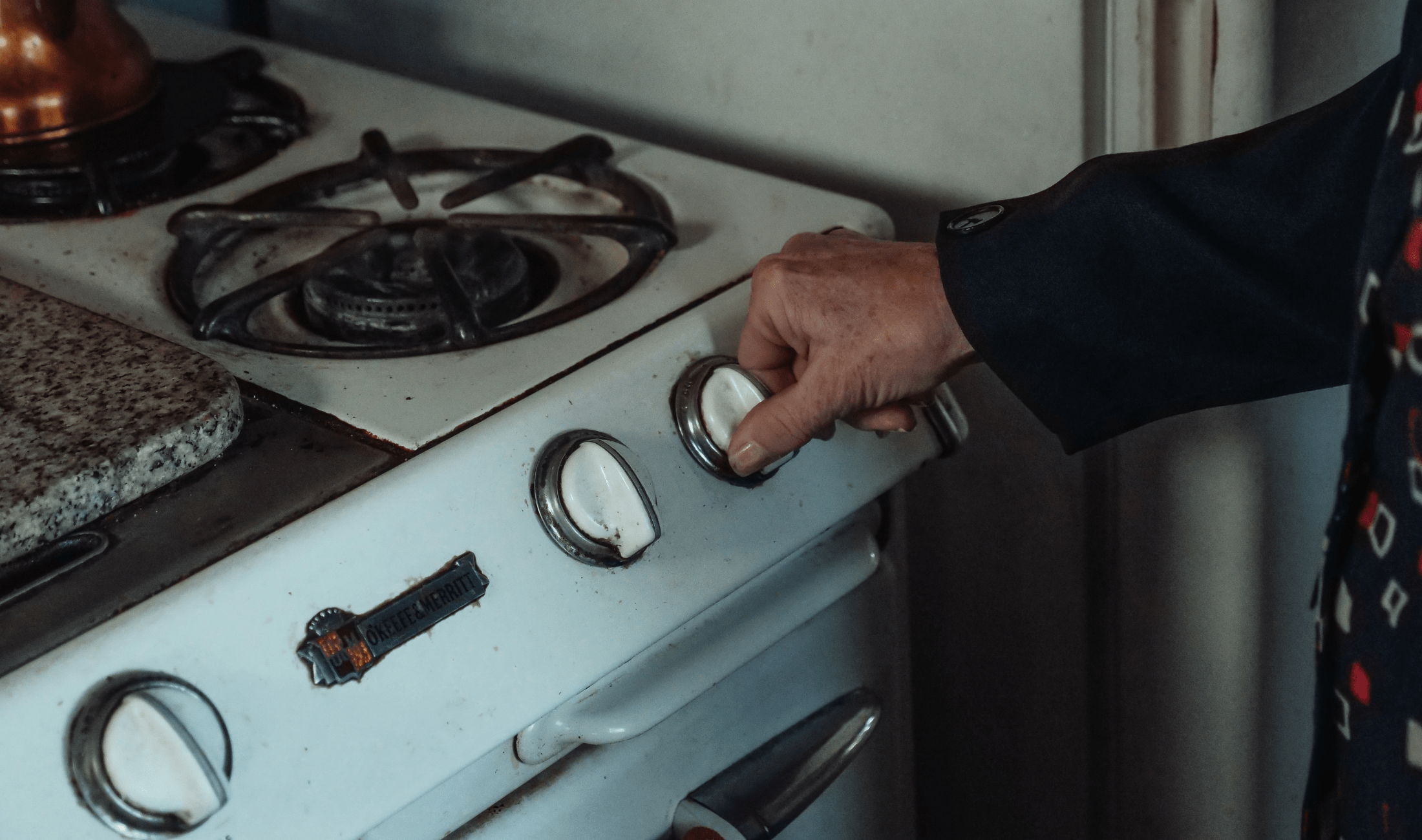 A woman's hand turning a knob on a stove.