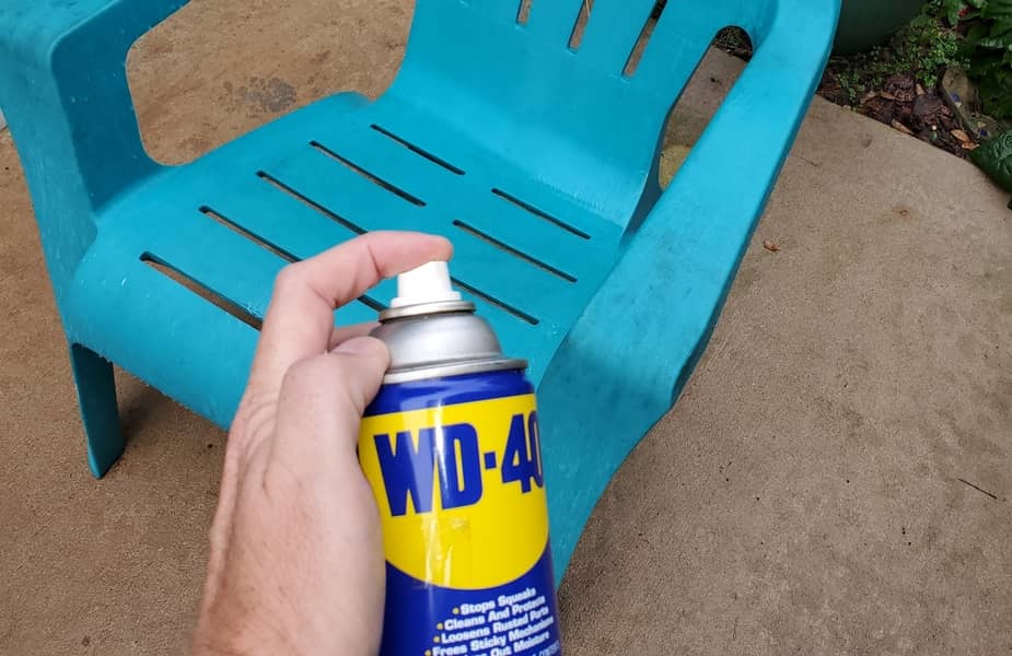 Someone holding a can of WD-40 above a blue plastic Adirondack chair.