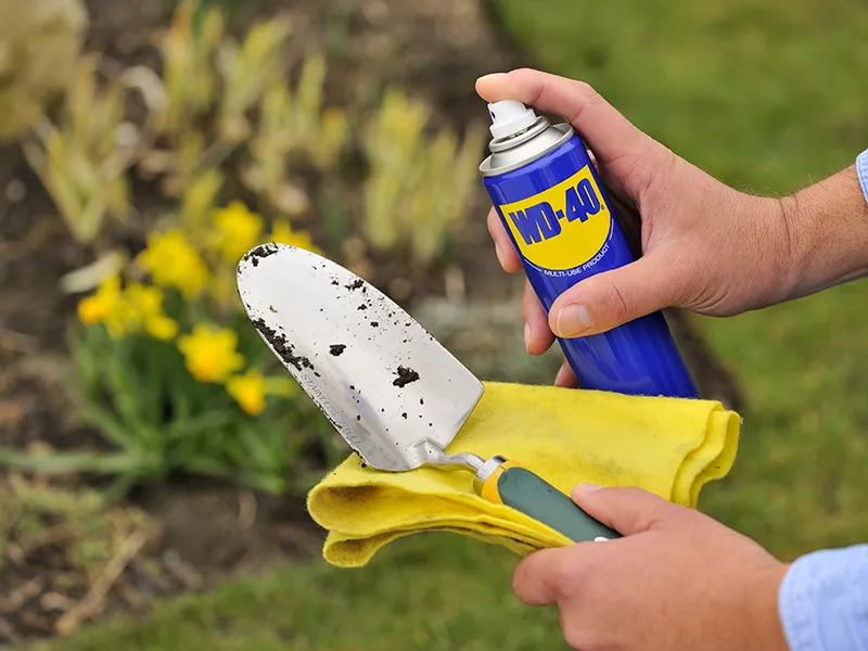 Someone holding a can of WD-40 by a trowel.