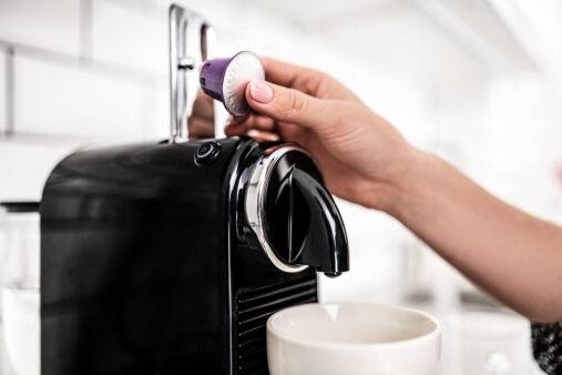 Girl hand put capsule to coffee machine at home closeup. Woman preparing italian caffeine beverage using professional espresso maker
