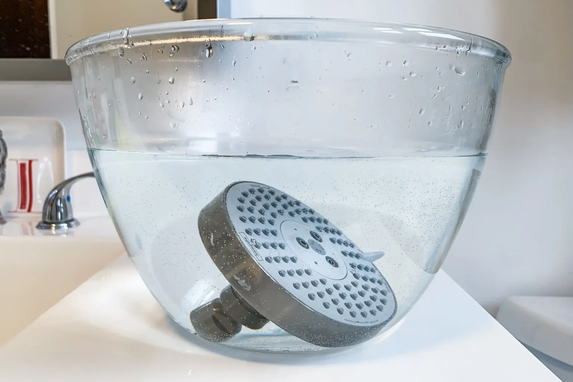 A showerhead sitting in a large glass bowl of vinegar.