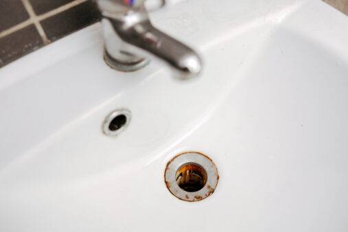 Dirty and rusty washbasin, close up view. Metal drain hole with red rust stain. Corrosion, unsanitary. Stained bathroom plumbing.