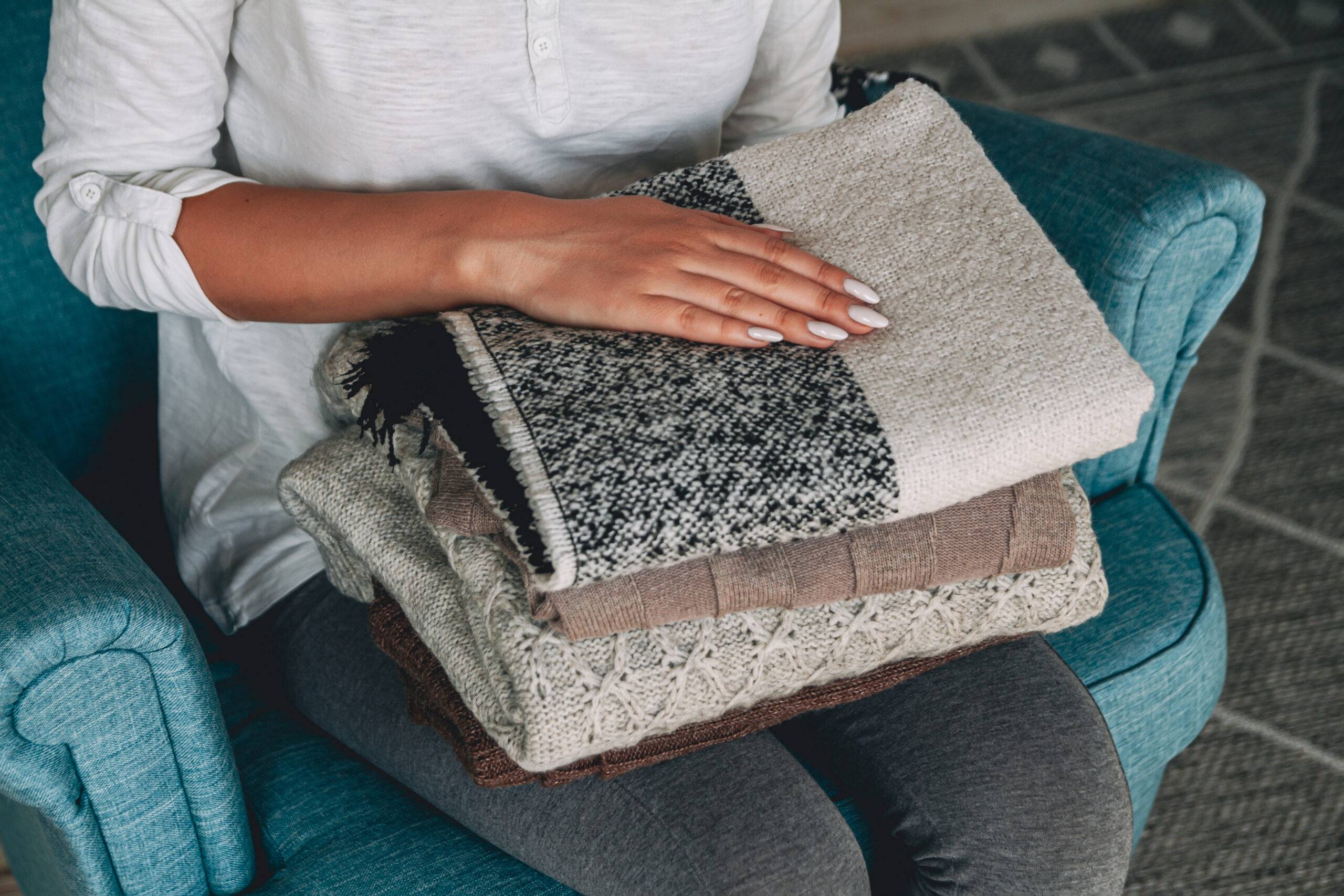 Female hands hold the stack of warm knitted sweaters