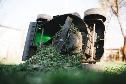 Lawn mower overflowing with grass lies on its side