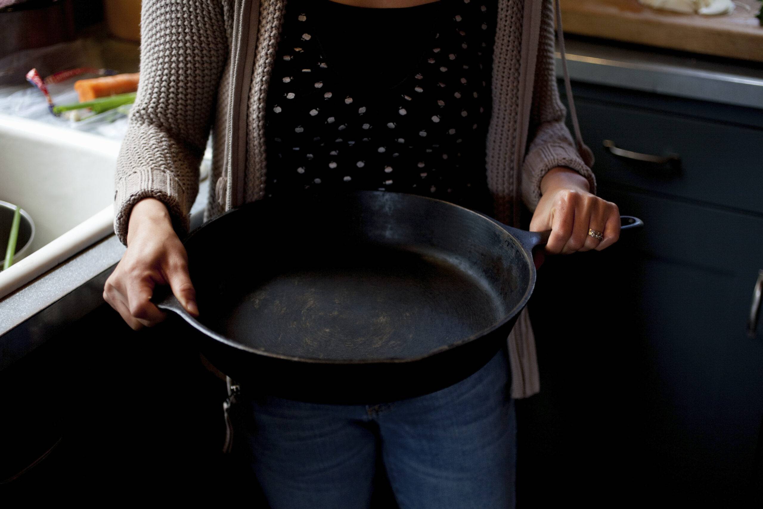 Woman holding empty skillet next to a sink.
